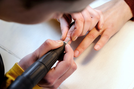 Hardware manicure in a beauty salon. Manicurist is applying  electric nail file drill to manicure on female fingers.の写真素材