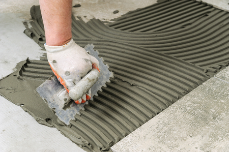 Laying Ceramic Tiles. Troweling mortar onto a concrete floor in preparation for laying  floor tile.の写真素材