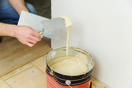 Laying hardwood parquet. Worker puts glue on the floor.