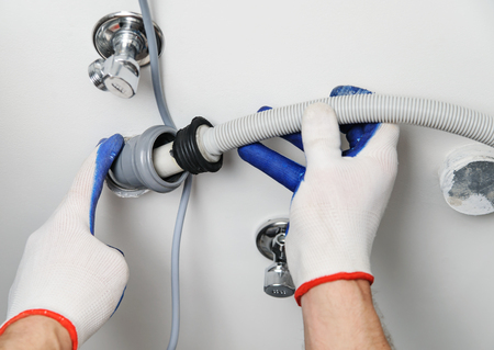 Installation of household appliances. Workman attaches a drain hose to a sewage pipe.の写真素材
