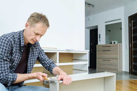 Mounting the chest of drawers. The  man is using a hammer to fix the drawer's boards.の写真素材