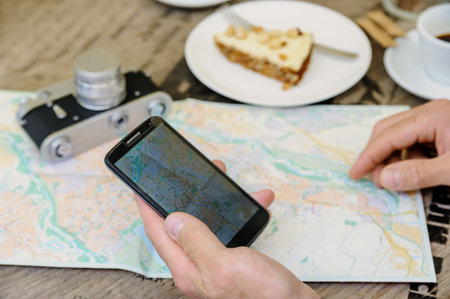 A man is holding a smartphone. He is sitting at the cafe table on the street. On the table there is...
