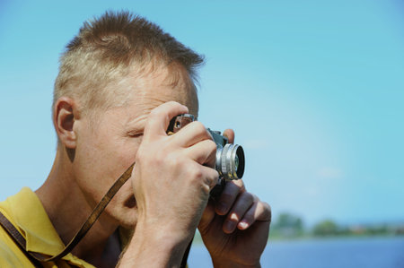 The man is photographing an old camera on a tree and lake background.