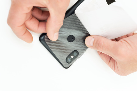 A man is glueing a protective carbon film on the back of the smartphone.の写真素材