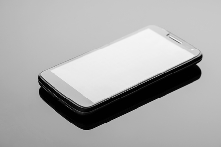 Modern smartphone on a dark glossy surface with reflection.の写真素材