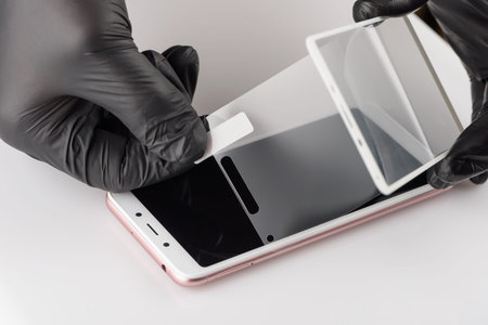A man is installing a protective glass on the screen of a smartphone.