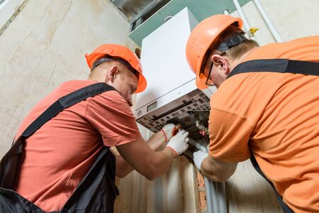 Workers are connecting the heating system pipes to the gas boiler.の写真素材