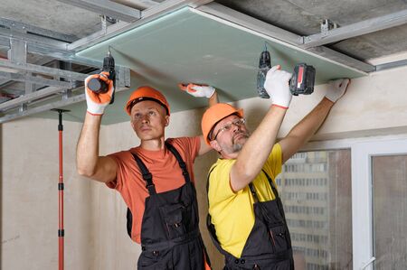 Workers are using screwdrivers to mounting plasterboard to the ceiling.の写真素材
