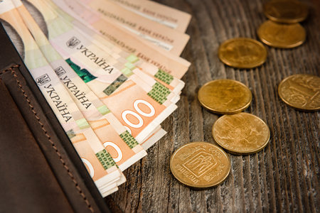 Brown leather wallet with banknotes and coins on old wooden surface. Close up.