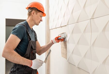 Installation of gypsum 3D panel. The worker is applying adhesive to the wall to attach the gypsum tile.の写真素材
