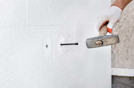 Insulation of the house with polyfoam. A worker is using a hammer for dowels that fasten polystyrene boards.の写真素材