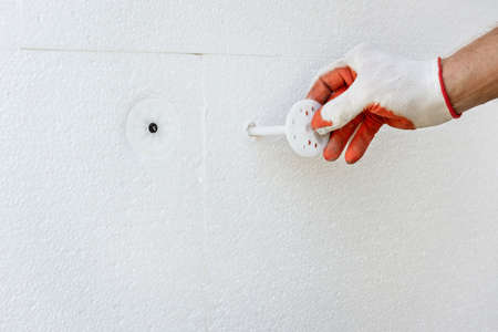 Insulation of the house with polyfoam. The worker is fixing a polystyrene board with plastic dowels.の写真素材