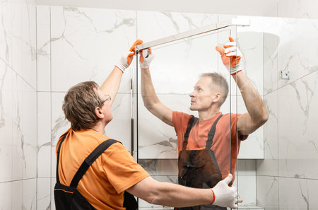 Workers are installing glass door of the shower enclosure.