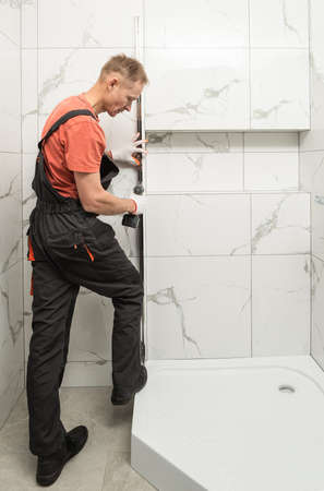 The worker is installing a metal profile of the shower cabin with a screwdriver.の写真素材
