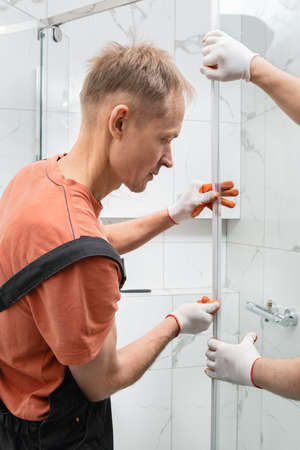 Workers are installing a silicone gasket seal on the glass door of the shower enclosure.の写真素材