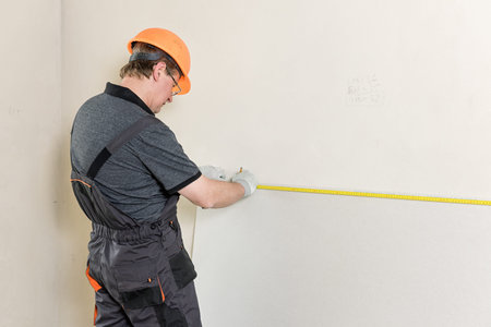 Installation of drywall. The worker is measured to cut off a piece of drywall later.の写真素材