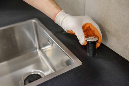 A plumber is setting the start button for the waste shredder on the kitchen sink.の写真素材