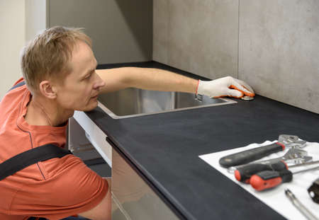 The plumber is setting the start button for the waste shredder on the kitchen sink.の写真素材