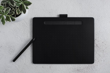 The graphic tablet with a stylus on a white background. There is a plant in a white pot nearby.の写真素材