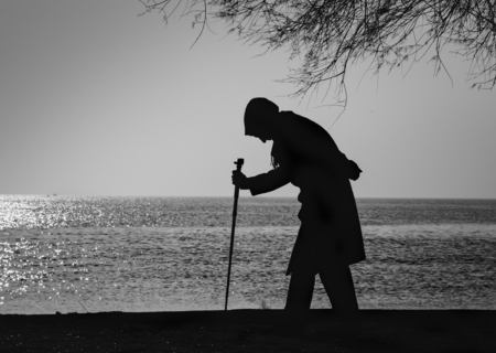 Old woman who walks on the beach walking stick between old treesの写真素材