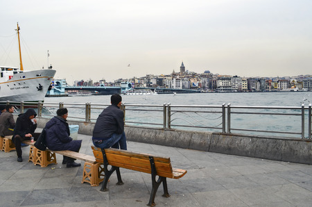 Istanbul, Turkey - February 21, 2013: Istanbul view. Eminonu pier, Galata bridge and Galata tower. People are resting on the bench.のeditorial素材