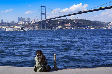 Istanbul, Turkey - March 10, 2013: View of the European side of Istanbul from the Bosphorus. On the shore watching a woman views. The Bosphorus Bridge (Turkish: Bogazici Koprusu), also called the First Bosphorus Bridge, is one of two suspension bridges spのeditorial素材