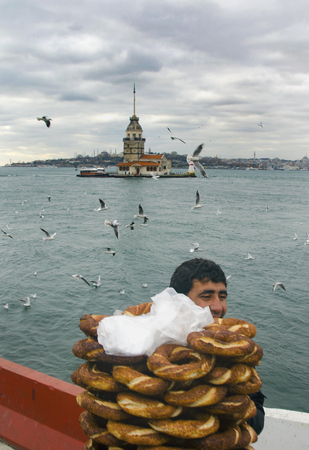 Istanbul, Turkey - December 04, 2013: Maiden Tower. A young salesman (Simit) bread vendor. European part of Istanbul in the background against the shore. Left Blue Mosque, medium Hagia Sophia, Topkapi palace dome seem right. The Maiden's Tower (Turkish: Kのeditorial素材