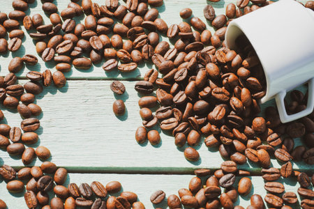 Roasted coffee beans and white cup on the wooden background.