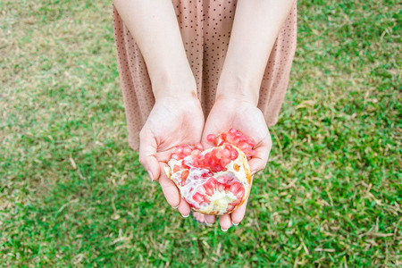 close up red pomegranate fruit in hands of woman standing on the groundの写真素材