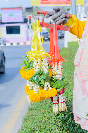 A man selling Thai garland offering on the road at traffic junctionの写真素材