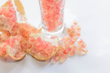 One whole and pieces of broken-up pomegranate fruit on wooden table with A champagne glass filled with ripe pomegranate fruit seeds and jarの写真素材
