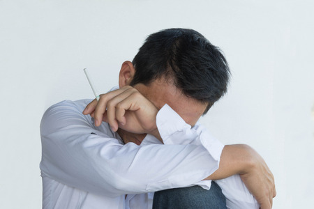 stressful businessman smoking an cigarette with lower head on his knee on white backgroundの写真素材