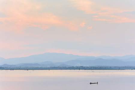 small fishing boat in the lake with mountain view against sunset skyの写真素材