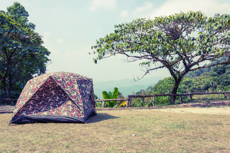vintage style photo of tent on ground with tree, mountain and blue sky background at Natural Parkの写真素材