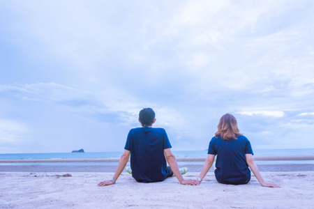 A couple holding hand and setting on the beach with blue sky backgroundの写真素材