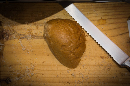 slice wheat bread with knife on wooden table with shadow edge