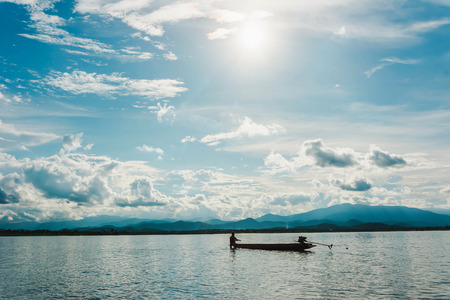 silhouette of fishing boat flooding on lake with mountain background at sunsetの写真素材