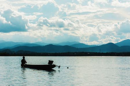 silhouette of fishing boat flooding on lake with mountain background at sunsetの写真素材