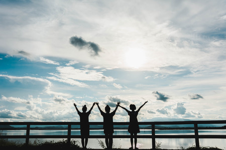 silhouette of young girls stand at fence at sunset with light and lake view backgroundの写真素材