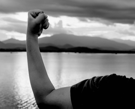 strong man's arm muscle against lake and mountain view with cloudy sky in white toneの写真素材