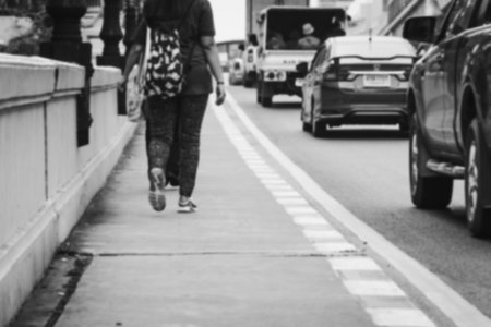 blurry photo of people walking to work on footpath by street with car on road in white toneの写真素材