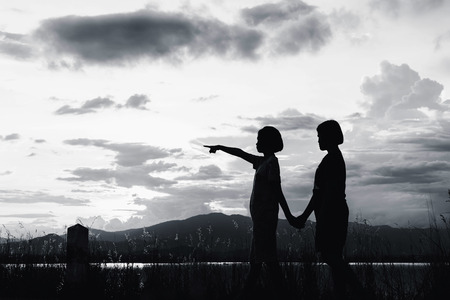 silhouette of girls pointing to sky at sunset in white toneの写真素材