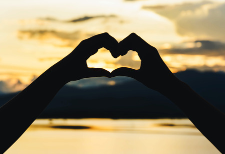 silhouette of girl's hand in heart  form at sunset. Hands in shape of love heartの写真素材