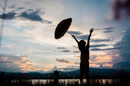 silhouette of young girls standing with umbrella at sunsetの写真素材