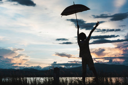 silhouette of young girls standing with umbrella at sunsetの写真素材