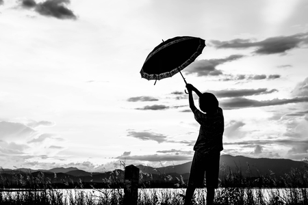 silhouette of young girls standing with umbrella at sunset in white toneの写真素材