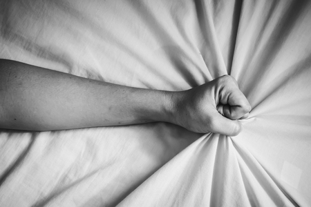 young woman in bed clutching tightly her Bed linen in white tone with shadow edgeの写真素材