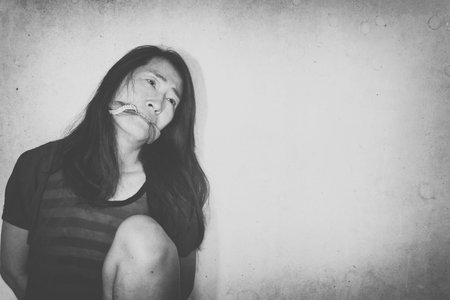 abused woman sitting on ground  with and hand and mouth tied with shadow edge, dirt effect, in white...