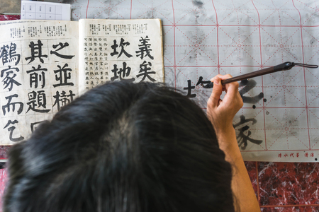 girl practicing chinese callingraphy using a brush pen in her handの写真素材