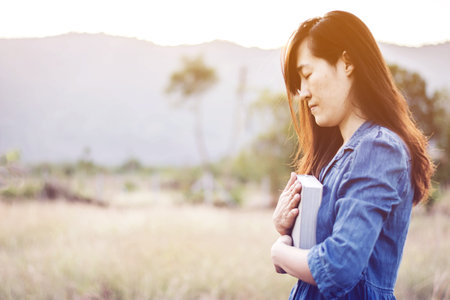 Woman praying in meadow at sunset with gradientの写真素材
